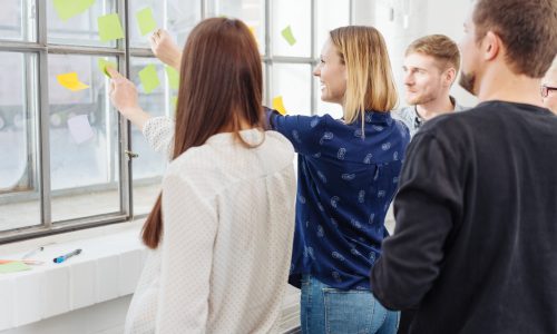 Motivated group of young business people Motivated group of young business people gathered around colorful sticky notes on an office window smiling as they discuss new ideas